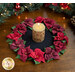 Photo to of the finished Poinsettia Wool Table Topper on brown wooden table with decorative garland in the background and a rustic candle at the center.