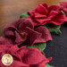 Close up image of the floral edge of the wool table topper showing layered wool to form red petals with green leaves on a black background