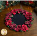 Photo to of the finished Poinsettia Wool Table Topper on brown wooden table with decorative garland in the background.