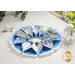 Flower shaped table topper on a white table top with a glass jar of fresh flowers and plants in the background. Topper is made of white and blue floral fabrics with green accents.