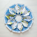 Flower shaped table topper on a white table top made of white and blue floral fabrics with green accents.