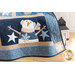 Close up of the bottom right of the draped quilt showing stitching detail with a snowman with arms raised wearing earmuffs with star accents over a brown wooden floor with a white paneled wall and a white lantern in the background