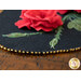 Close up of a black oval table topper with 3-dimensional roses and green leaves with gold beads around the edge on a brown wooden table