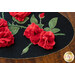 A black oval table topper with 3-dimensional roses and green leaves with gold beads around the edge on a brown wooden table