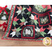Photo of finished Christmas Eve quilt made with red, green, black, and white fabrics draped in the foreground with a wreath and wrapped presents in the background