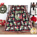 A finished Christmas Eve Quilt draped over a bench with a ladder shelf on the right featuring homey decor, and wrapped gifts on the other with a wreath hanging on the wall.