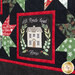 Close up of quilt blocks from the Christmas Eve Quilt showing traditional star designs using red, green, black, and white fabrics, and a panel block showing a house inside a wreath with the words 