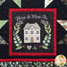 Close up of quilt blocks from the Christmas Eve Quilt showing traditional star designs using red, green, black, and white fabrics, and a panel block showing a house inside a wreath with the words 