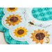 Close up photo of a white scalloped table topper with aqua plaid edges and center with simple applique sunflowers in a ring, accented by hand embroidered bee details