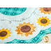 Close up photo of a white scalloped table topper with aqua plaid edges and center with simple applique sunflowers in a ring, accented by hand embroidered bee details