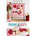 Photo of a finished wall hanging with a gnome dressed as cupid with a bow and arrow and heart motifs hanging on a metal craft hanger with a vase of flowers and potted flowers on either side and in front of a white paneled wall with the words 