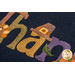 Close up of the Words in Wool November mat showing the applique detail of multicolored letters and a buckled hat on the letter 