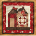 A finished quilt block depicting a house made with red and cream fabrics on a brown countertop.