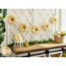 Photo of sunflower garland strung on a white trellis against a white wall with a brown and white farmhouse style countertop with yellow fabrics and a basket of yellow and white flowers with greenery and a beehive decoration