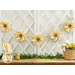 Photo of sunflower garland strung on a white trellis against a white wall with a brown and white farmhouse style countertop with yellow fabrics and a basket of yellow and white flowers with greenery and a beehive decoration