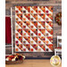 Photo of a geometric quilt with small stars in each block, made with autumn themed fabrics hanging on a dark wood paneled wall with autumn floral decor and painted white furniture on either side.