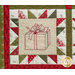 Close up of one quilt block showing fabric and stitching detail with an embroidered image of a wrapped gift adorned with a bow and holly