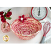 Photo of a bowl made from coiled red and cream colored fabrics with a red fabric flower sitting on a white countertop with a red whisk, scale, and pink bottle with red roses in it.