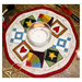 Photo of finished candle mat project featuring a round mat with traditional quilt block patterns overlapping in the ring, and a lit candle at the center