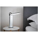 A white foldable lamp at a 90 degree angle on a white marble bedstand next to a bed and pillows