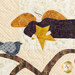 Close up photo of an angel motif at the top of the quilt, holding a start and flying next to a bird perched in a tree