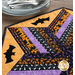 Close up photo of the Spooky Hallow table topper showing fabric details and bat motifs with a stack of plates and forks in the background