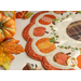 Close up photo of a scalloped table mat with pumpkins in a ring and embroidered details on a white table with acorns, leaves, and pumpkin decor