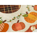 Close up photo of a scalloped table mat with pumpkins in a ring and embroidered details around a brown plaid circle at the center