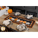 Photo of a Halloween themed table runner made with black, orange, and white fabrics with points along the top and bottom and a row of pumpkins in the center, on a wooden table top with pumpkins and Halloween decor atop four place settings