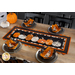 Photo of a Halloween themed table runner made with black, orange, and white fabrics with points along the top and bottom and a row of pumpkins in the center, on a wooden table top with pumpkins and matching bowl cozies atop four place settings