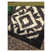 Photograph of the finished Rising Star Quilt, a black and white geometric log cabin quilt, draped from a bench in a park