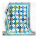Photograph of the finished jelly roll blues quilt with blue, green, and white fabric against a white wall