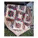 Photograph of the finished Country Retreat Log Cabin quilt in tan, brown, and red, hung from a fence on a green lawn
