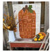 Photograph of a white quilt with a tall, orange pumpkin quilted onto it, surround by farmhouse wood and fall decorations