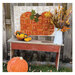Photograph of a white quilt with a wide, orange pumpkin quilted onto it, surround by farmhouse wood and fall decorations
