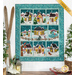 A teal, winter-themed quilt with houses, snowmen, and other winter imagery in 9 blocks, each of the 3 rows creating a winter scene. Quilt is hanging on a white paneled wall with winter decor all around.