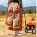 Close up of the log cabin throw quilt made with orange, brown, and cream fabrics draped over the arm of a woman wearing a green coat who is pulling a red wagon filled with pumpkins through a field with mountains in the background