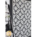 Photo of a black, white, and gray geometric quilt hanging flat against a wall in a room with monochromatic decor such as a small black house, black ladder-style shelf, and white flowers in a silver vase.