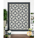 The completed Lattice Bouquet Quilt in Steelworks, rich shades of cool, smoky, and medium gray fabrics, hung on a white paneled wall and staged with coordinating furniture and decor.
