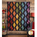 Photo of the Scintillation flannel quilt made with rainbow colored fabrics and black accents hanging on a brown paneled wall with a shelf and brightly colored decor on one side and a lamp with a red shade on the other