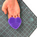 purple silicone heart cutting mat scrubber being held by a person over a cutting mat