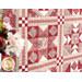 Close up photo of a large red and cream patchwork quilt hanging flat on a wall with a bouquet of red and white flowers in the foreground