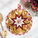 Close up photo of a round folded star hot pad made with yellow, white, and red floral fabrics laying flat on a white countertop with wooden spoons and a bouquet of flowers