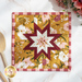 Close up photo of a square folded star hot pad made with yellow, white, and red floral fabrics laying flat on a white countertop with wooden spoons and a bouquet of flowers