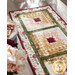 Close up photo of a table runner made with log cabin blocks and cream, yellow, green, and red floral fabrics with a stack of plates and bouquet of flowers in the foreground