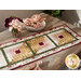 Photo of a table runner made with log cabin blocks and cream, yellow, green, and red floral fabrics with a stack of plates and bouquet of flowers in the background
