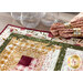 Close up photo of a table runner made with log cabin blocks and cream, yellow, green, and red floral fabrics with matching napkins and short glasses in the background