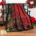 The completed Poinsettia Kaleidoscope quilt, artfully draped over a dark bench and staged with coordinating furniture and decor.