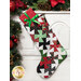 Photo of a Christmas stocking made with red, green, black, and white Christmas fabrics hanging from a white mantle with garland all around and a red wrapped gift inside the stocking.
