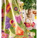 Photo of the colorful floral quilt Full Bloom hanging in the foreground with a blonde woman sitting in the background with a basket of flowers and small white dresser